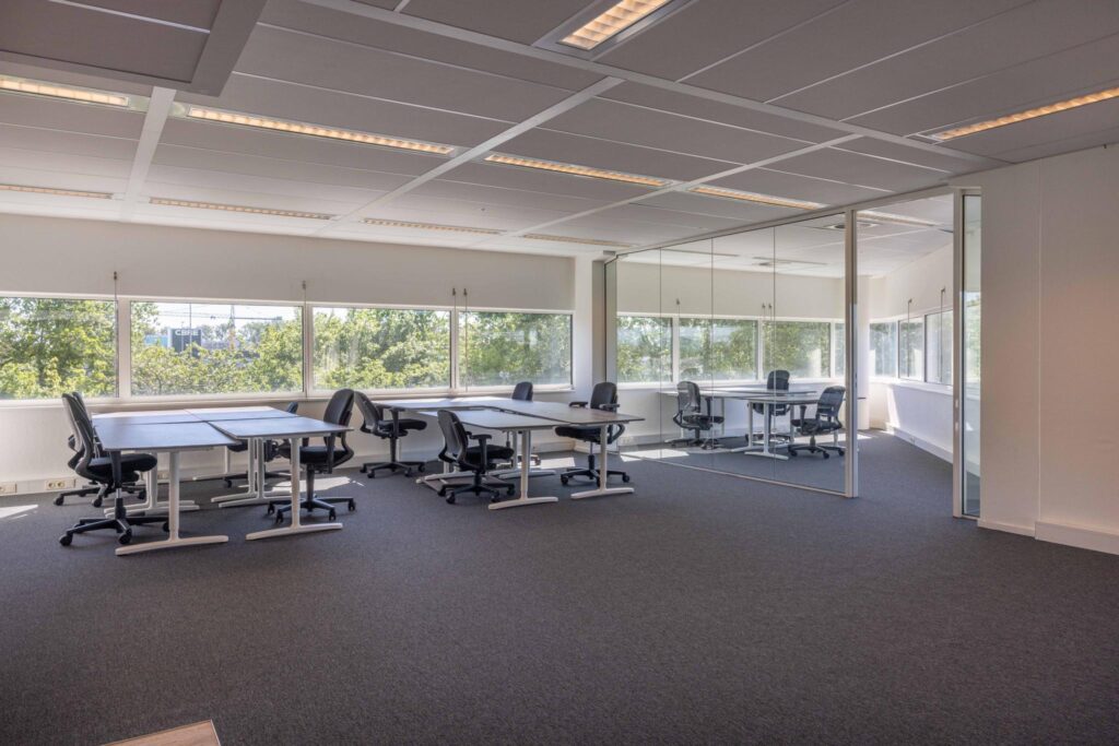Modern office space on Overschiestraat with large windows, multiple desks, and a glass-walled meeting room.