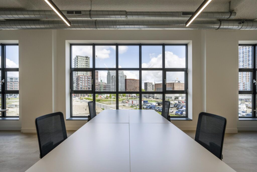 Modern meeting room with large windows offering a view of urban development and parked vehicles outside.