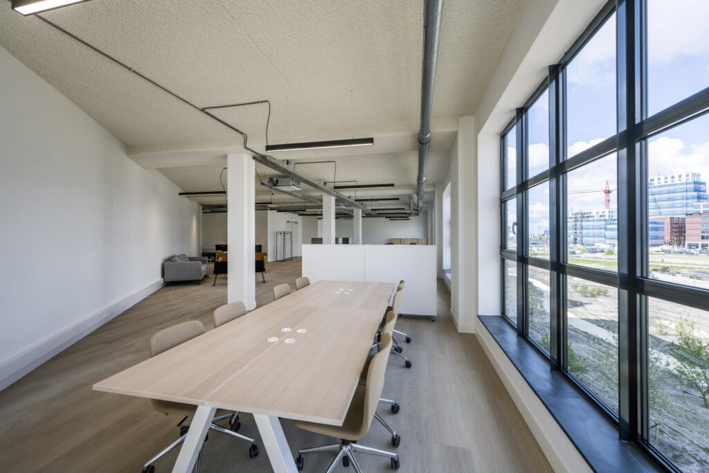 Modern open-plan office space with large windows and a long meeting table.