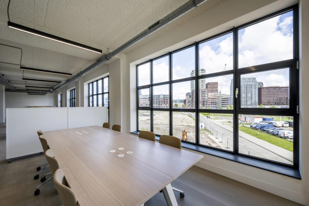 Modern office meeting room with large windows overlooking an urban construction site and city buildings.