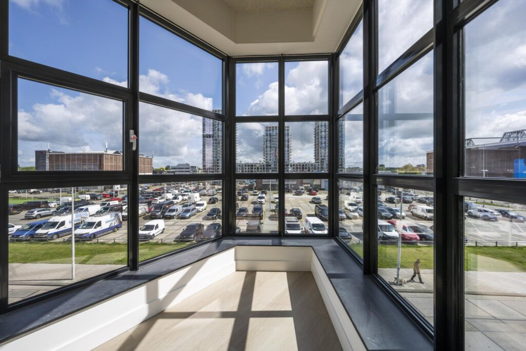 View from a corner window overlooking a large parking lot and modern high-rise buildings in the distance.