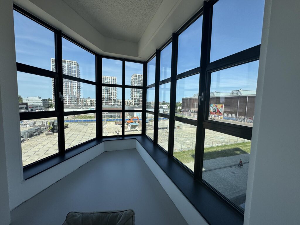 View from a corner window overlooking a construction site and modern high-rise buildings near the Hellingbaan area.