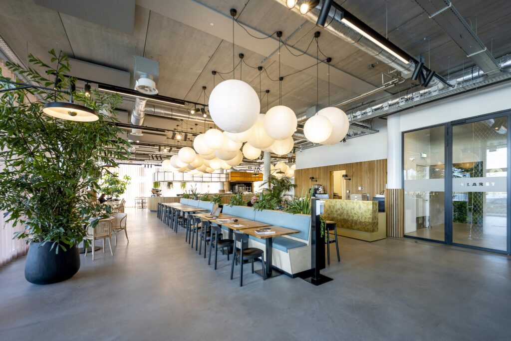 Modern office cafeteria at Moermanskkade with hanging paper lanterns, wooden furniture, and indoor plants.