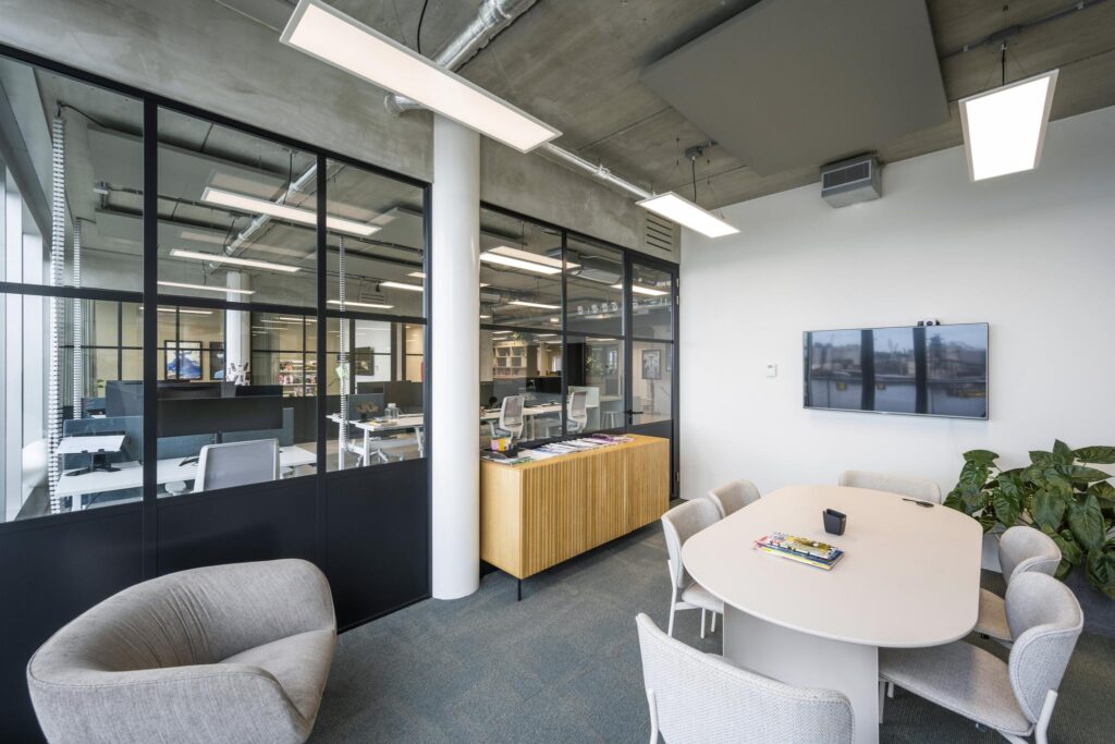 Modern meeting room at Moermanskkade featuring a conference table, comfortable chairs, a wall-mounted screen, and a view into an open office space.