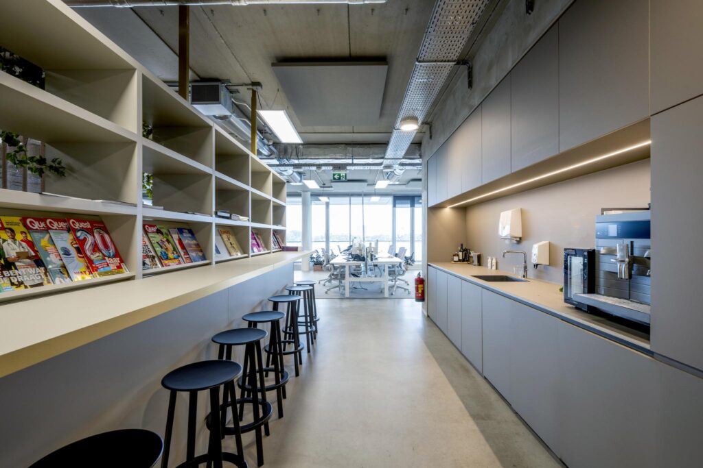 Modern office pantry with coffee machine, bar stools, and magazine shelf at Moermanskkade.