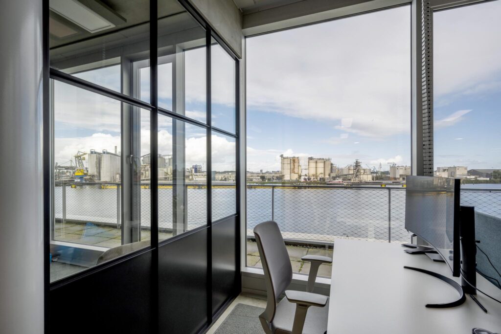 Modern office workspace with a waterfront view of Moermanskade industrial area through large windows.