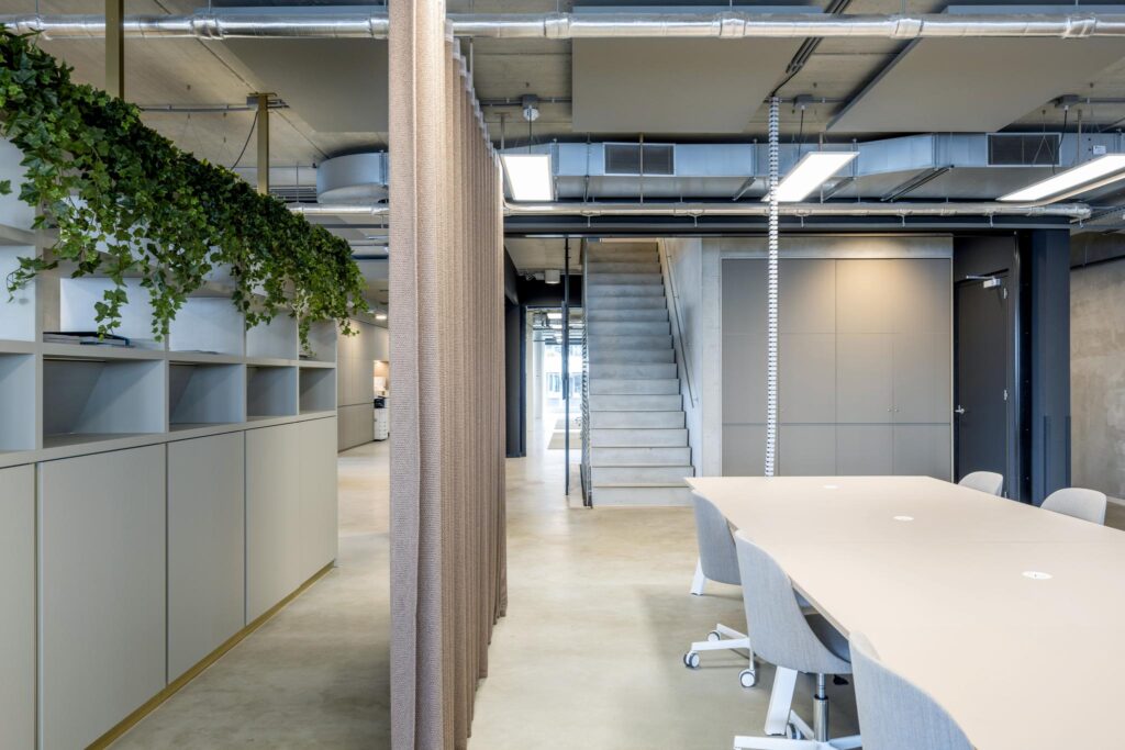 Modern office interior at Moermanskkade with a minimalist meeting table, open shelving, hanging plants, and an industrial-style staircase.