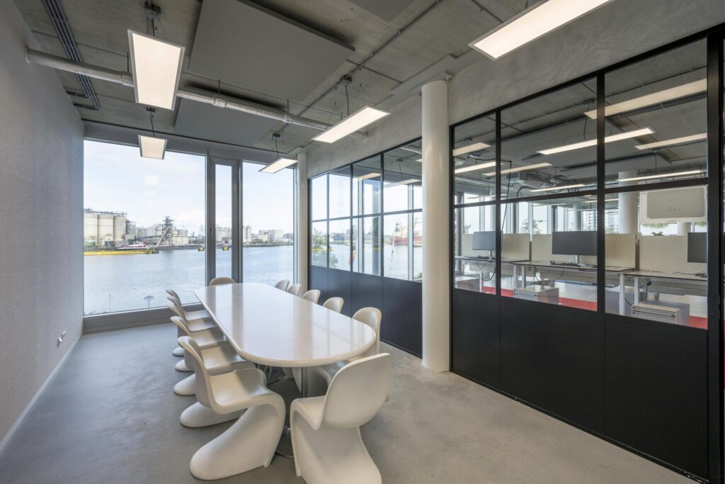 Modern meeting room at Moermanskkade with waterfront view and glass wall overlooking an open-plan office.