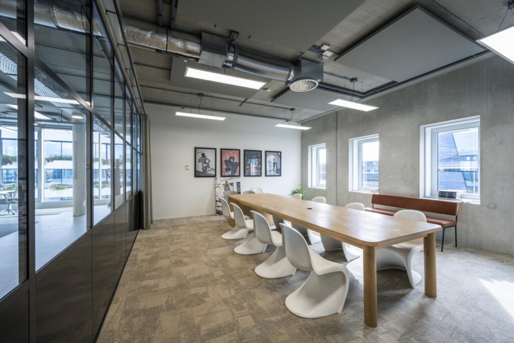 Modern conference room on Moermanskkade with a long wooden table, white chairs, industrial ceiling, and wall art.