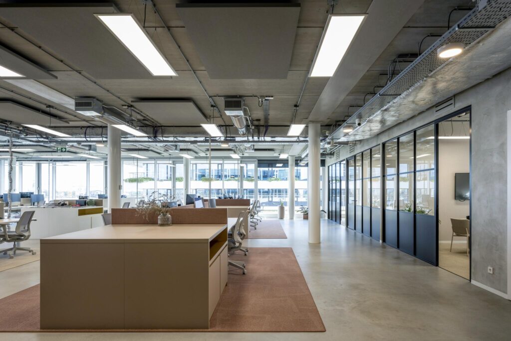 Modern open-plan office interior on Moermanskkade with workstations, glass meeting rooms, and industrial ceiling design.