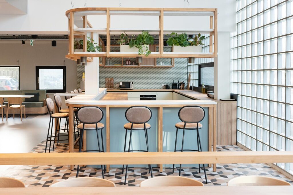 Modern communal kitchen area with high stools, light wood finishes, and hanging plants on Overschiestraat.