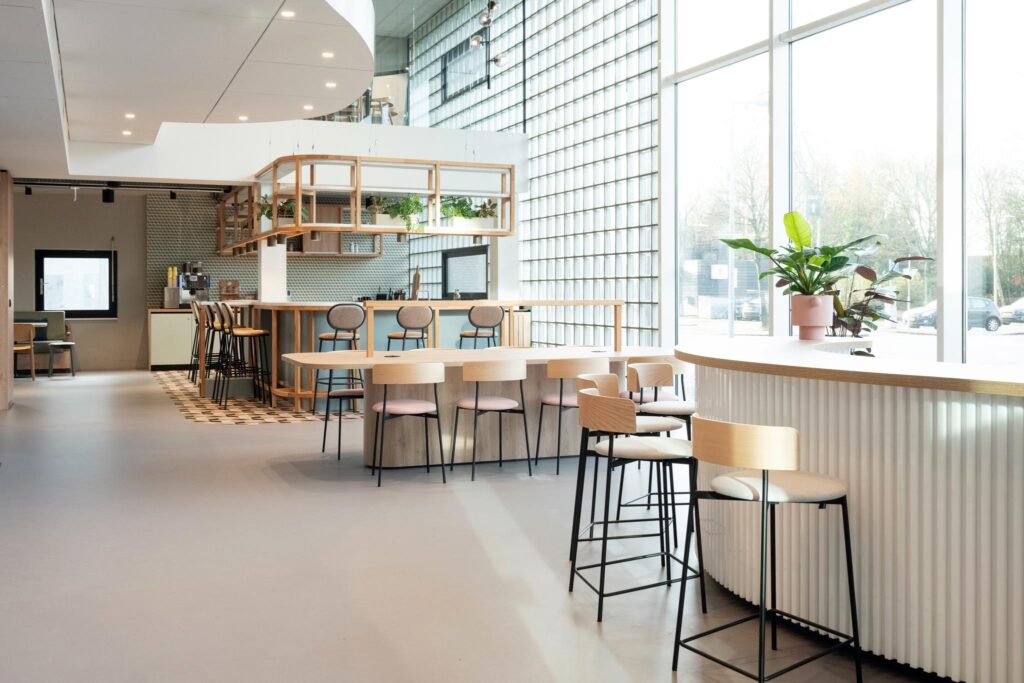 Modern shared workspace with a central bar, high stools, wooden tables, and large windows at Overschiestraat.
