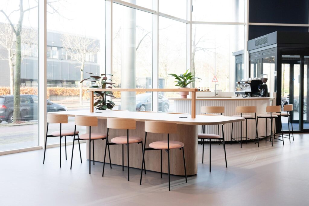 Modern office café area with large windows, wooden furniture, and a coffee bar on Overschiestraat.