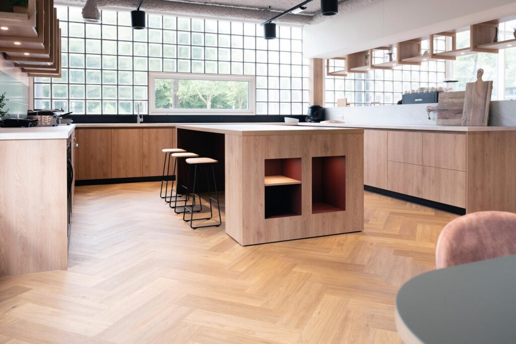 Modern open kitchen with light wood cabinetry, a central island with bar stools, and large glass block windows.