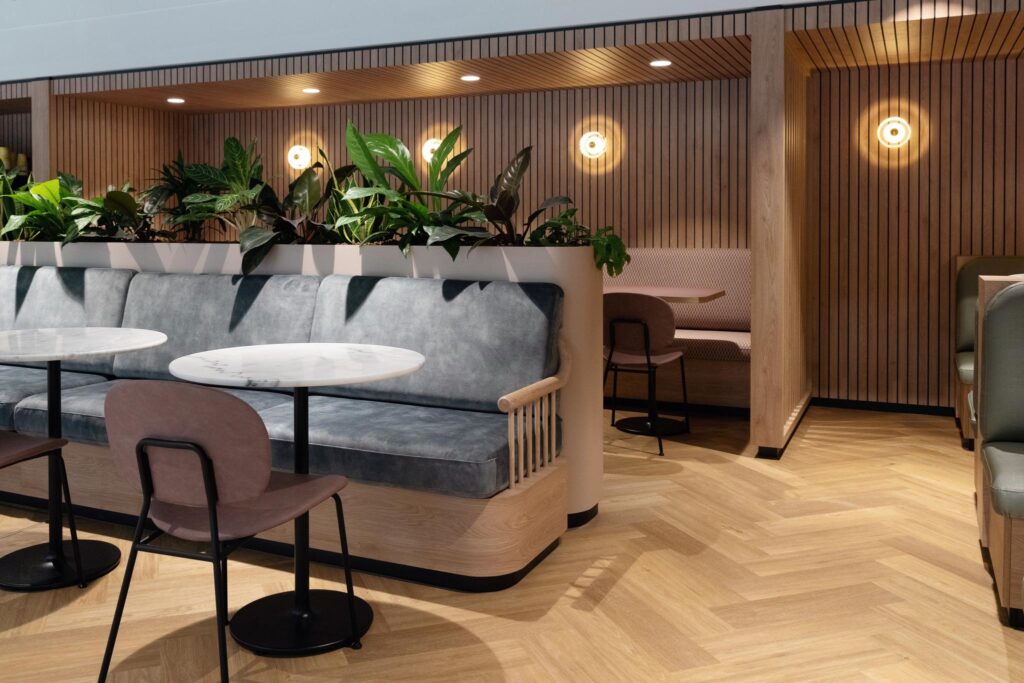 Modern seating area at Overschiestraat featuring soft benches, marble tables, wooden finishes, and indoor plants.