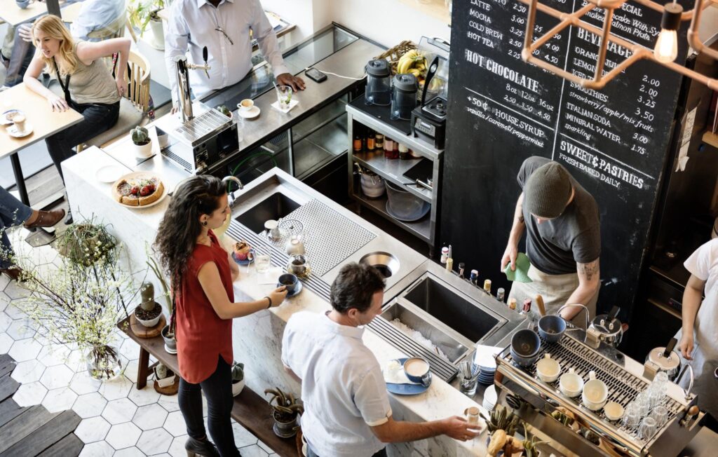 Busy café scene with baristas preparing drinks behind the counter and customers waiting at Bloemlaan.