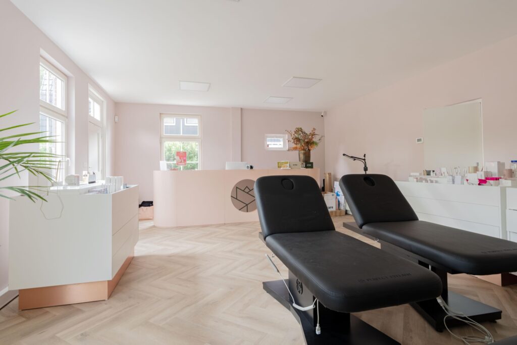 Modern treatment room at Sloterweg with two black wellness beds, a light pink reception desk, and minimalistic decor.