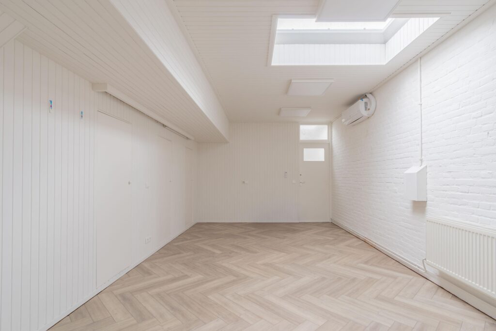 Bright white room with herringbone wooden flooring, skylights, and a wall-mounted air conditioner.