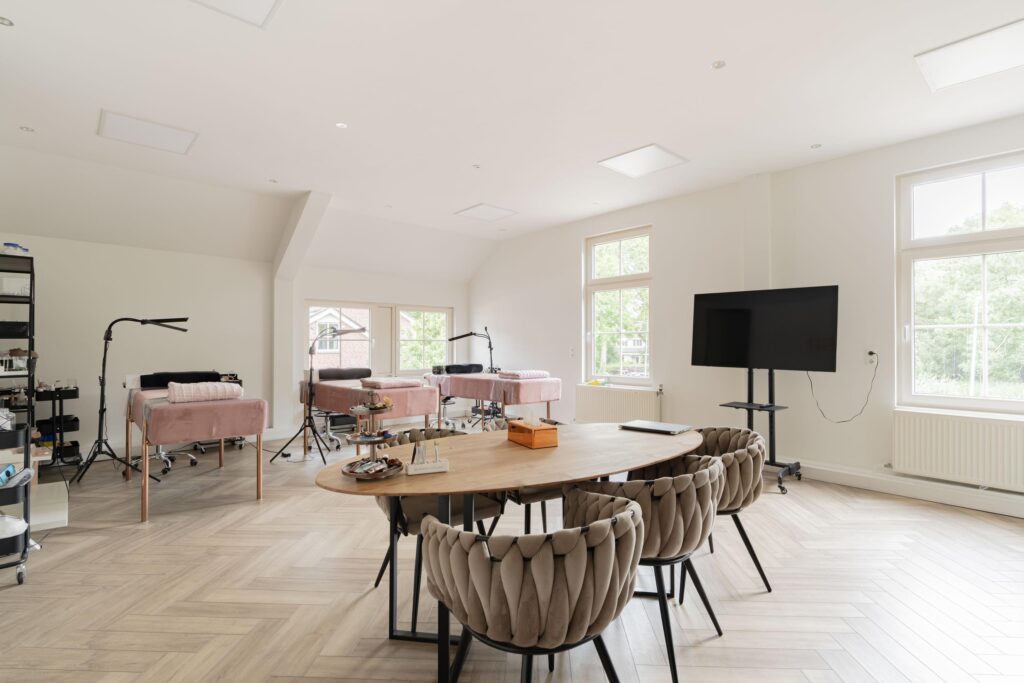 Modern beauty treatment room with multiple pink treatment beds, a wooden meeting table, and a large TV screen.
