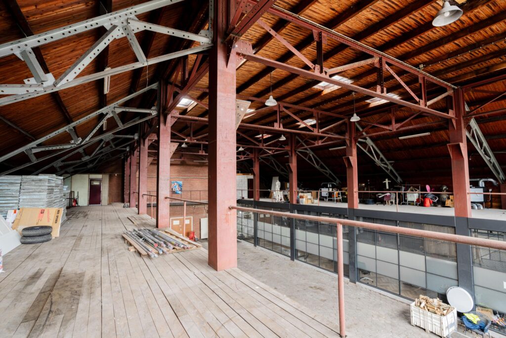 Industrial loft space with wooden floors, exposed beams, and storage and work areas along the mezzanine level.
