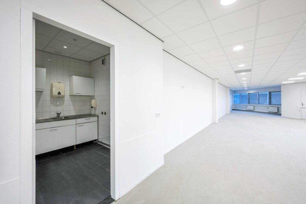 Witte kantoorruimte aan de Kuiperbergweg met kitchenette en groot raam aan het einde van de ruimte.