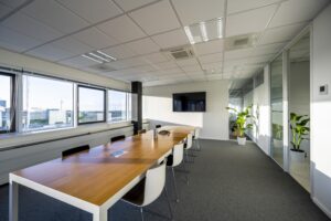 Moderne vergaderruimte aan de Kuiperbergweg met lange tafel, witte stoelen, grote ramen en een flatscreen tv aan de muur.