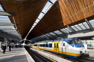 NS Sprinter-trein staat stil op een perron onder het moderne houten dak van station Arnhem Centraal.