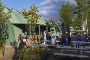 Mensen genieten van een drankje op het terras bij een groen gebouw aan de Kuiperbergweg.