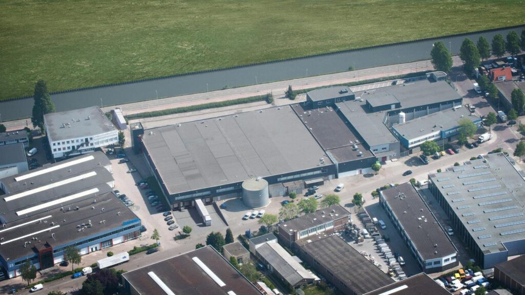 Aerial view of industrial buildings along Weesperstraat near a canal and green fields.