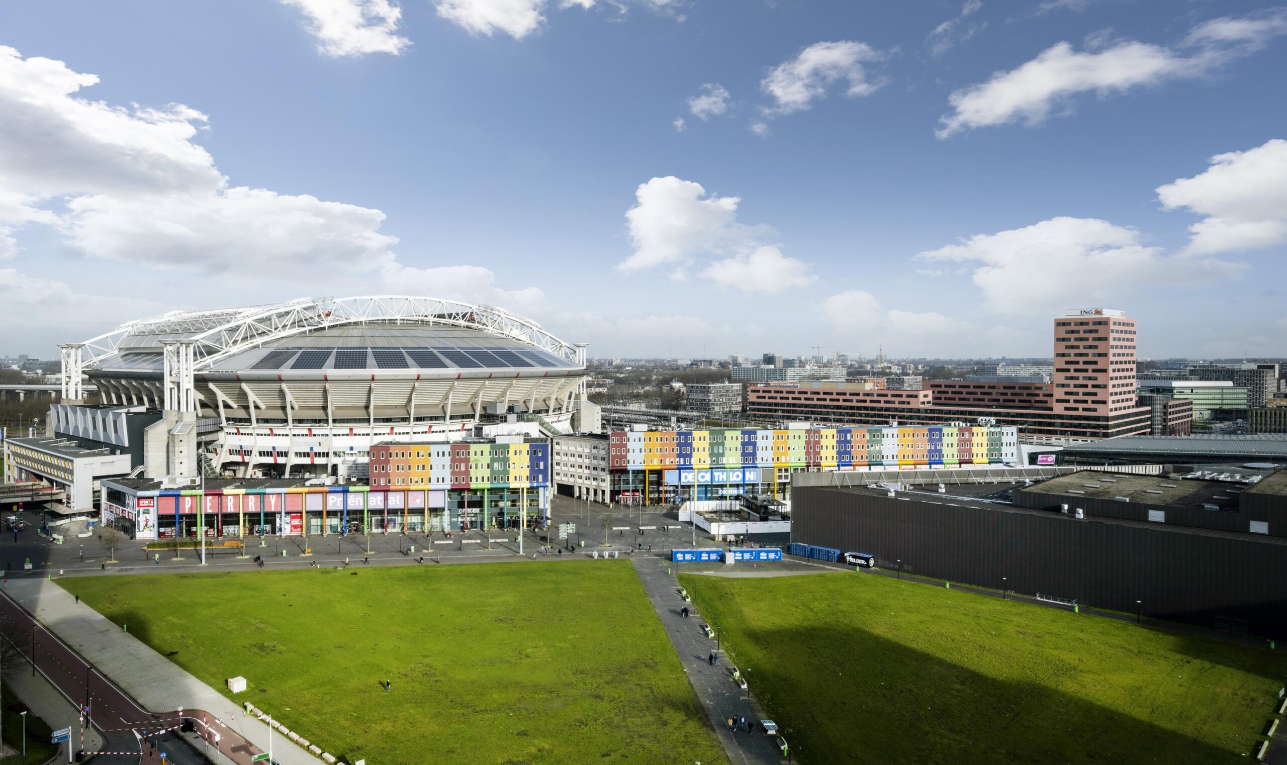 Exterior view of the Johan Cruijff ArenA and colorful shopping buildings along the Kuiperbergweg in Amsterdam.