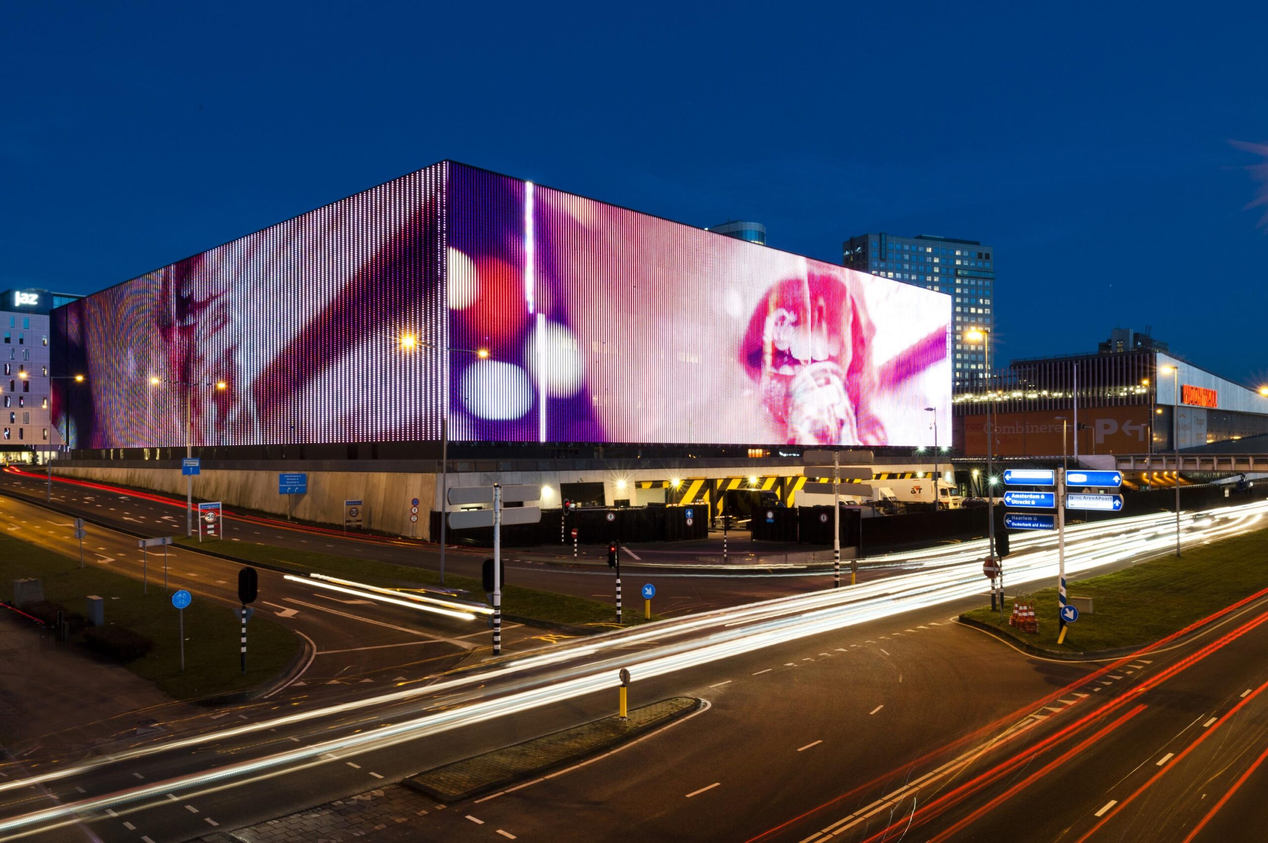 Large LED screen on Kuiperbergweg displays colorful visuals above a busy intersection at night in Amsterdam.