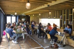 Mensen zitten aan tafels in een sfeervol, houten café aan de Kuiperbergweg, waar ze werken, praten en ontspannen.