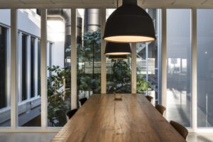 Vergaderruimte met houten tafel, hanglampen en uitzicht op een binnentuin met grote planten bij Kuiperbergweg.