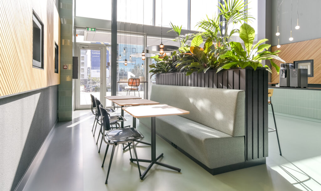 Modern office cafeteria at Paasheuvelweg with minimalist furniture, large windows, and indoor plants.