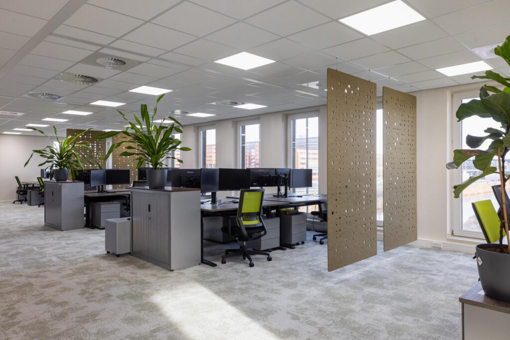 Modern open-plan office space at Paasheuvelweg with workstations, green office chairs, large windows, and decorative room dividers.