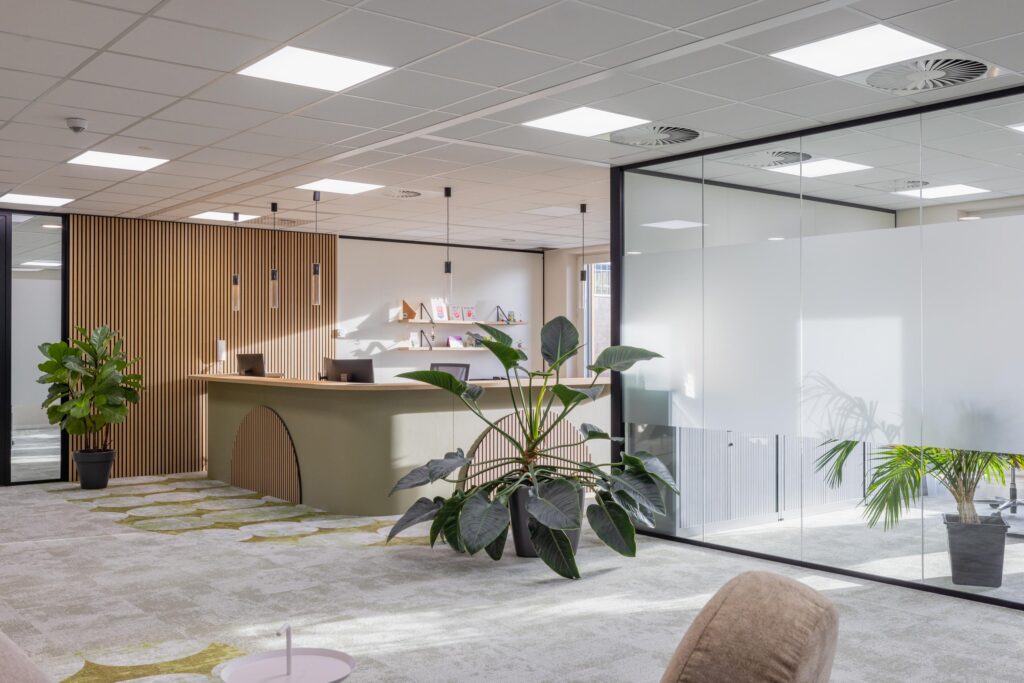 Modern office reception area at Paasheuvelweg with a curved desk, wooden slat wall, large indoor plants, and glass partition walls.