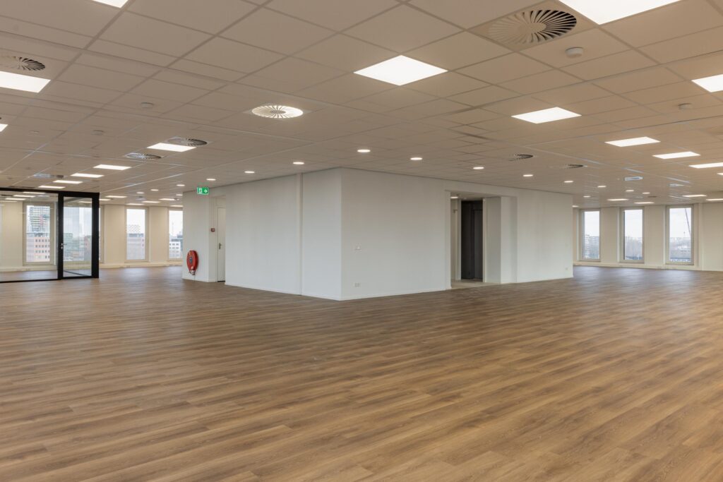 Modern empty office space at Paasheuvelweg with wooden flooring and large windows.