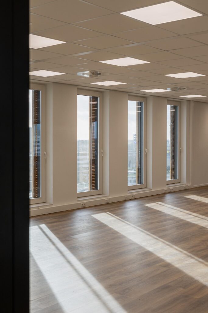 Bright, empty office space on Paasheuvelweg with large windows and wooden flooring.