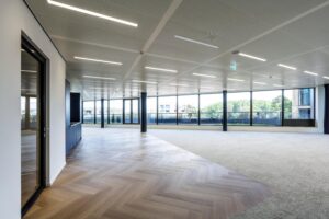 Modern open office space on Gelrestraat with large windows, herringbone wood flooring, and neutral carpeting.