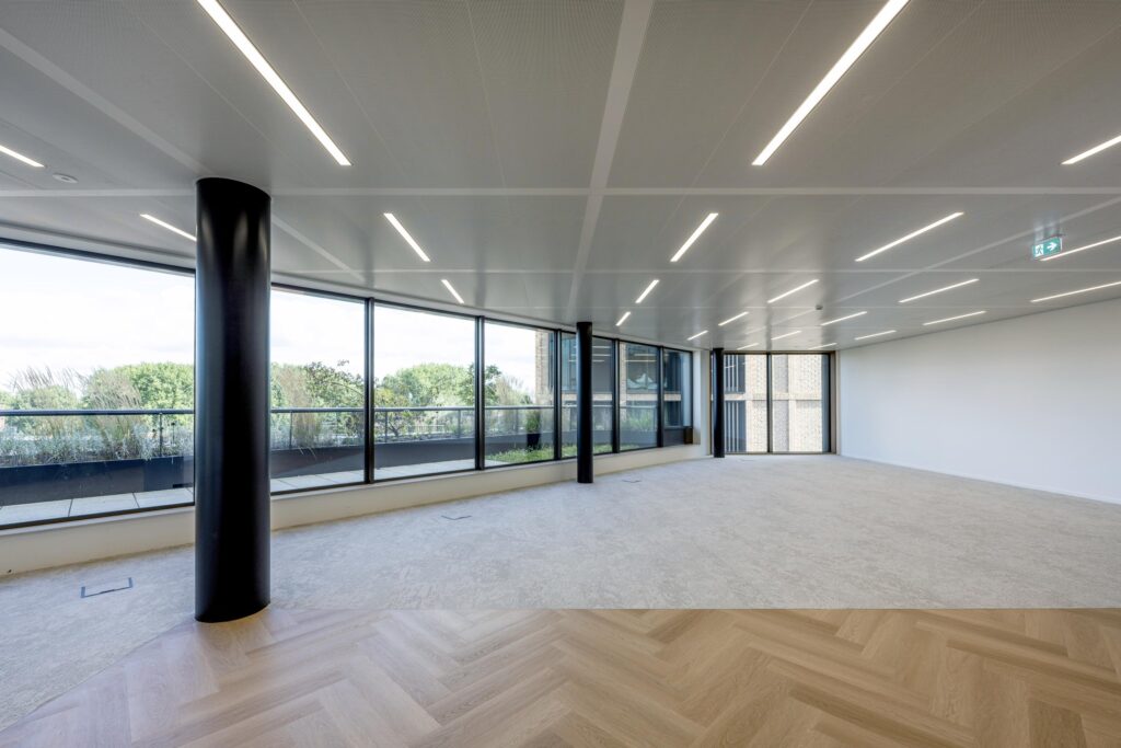 Modern empty office space on Gelrestraat with large windows, LED ceiling lights, and a mix of carpet and herringbone wooden flooring.