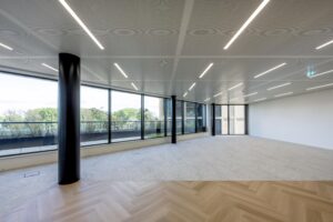 Modern empty office space on Gelrestraat with large windows, LED ceiling lights, and a mix of carpet and herringbone wooden flooring.