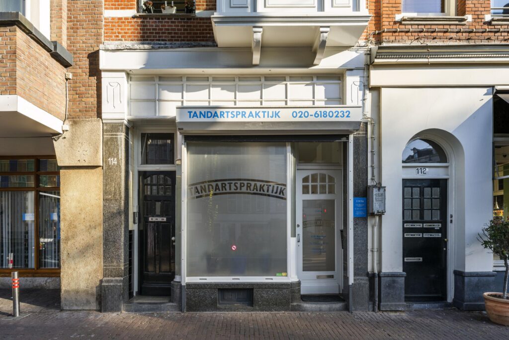 Street view of a dental practice at Overtoom 114 in Amsterdam with frosted windows and a blue sign above the entrance.