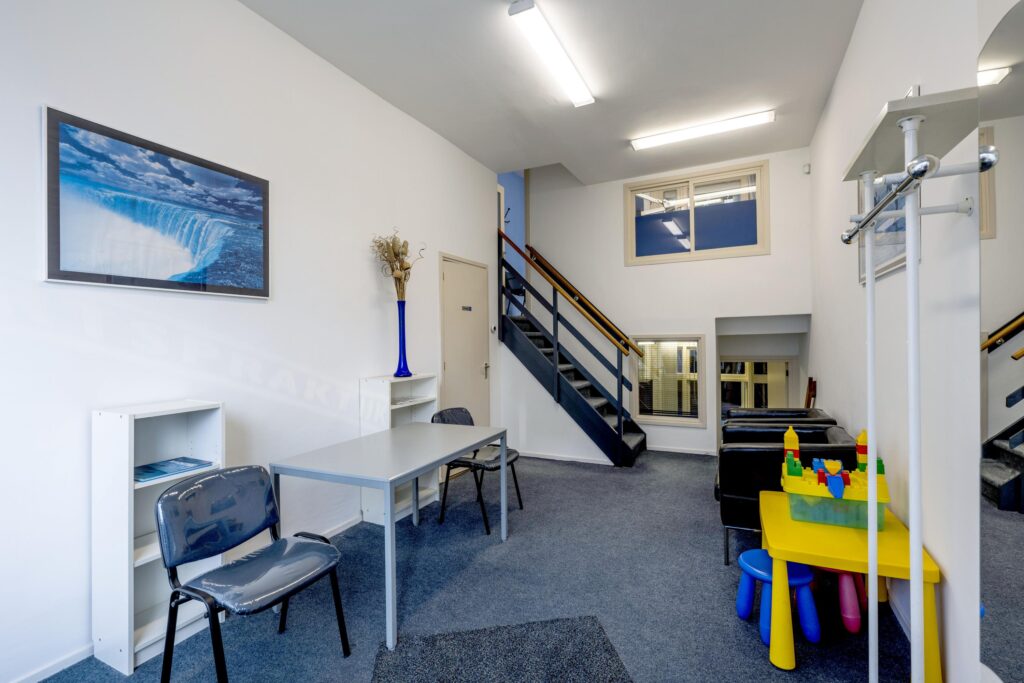 Waiting area with chairs, a children's play table, a staircase, and a waterfall picture on the wall.