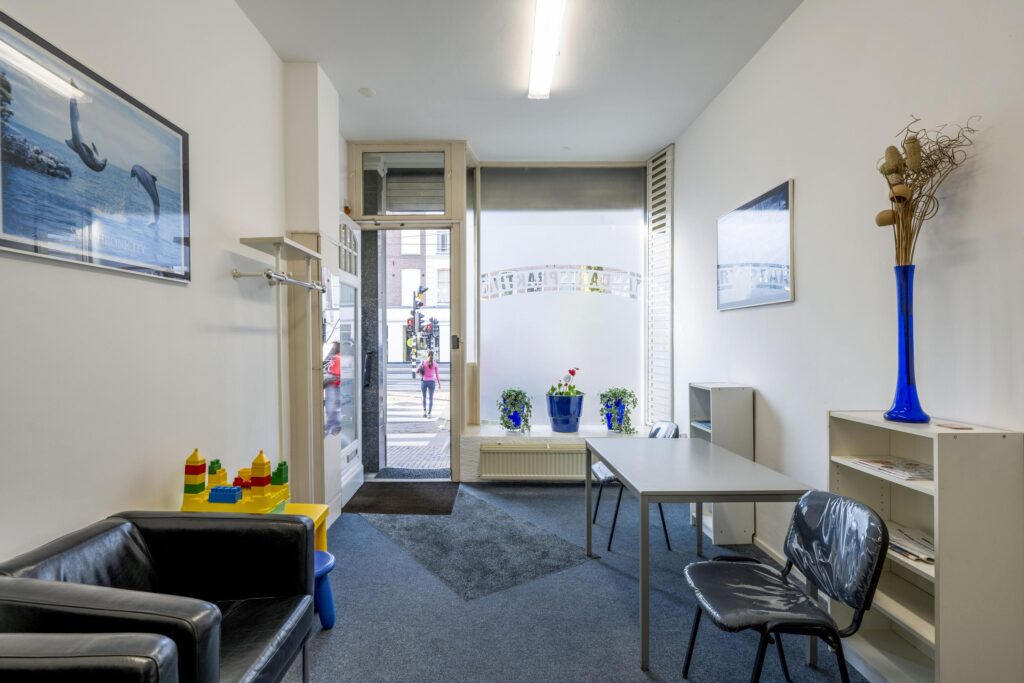 Waiting area at Overtoom 245 with simple furnishings, children's play table, and a view of the street through the glass front.