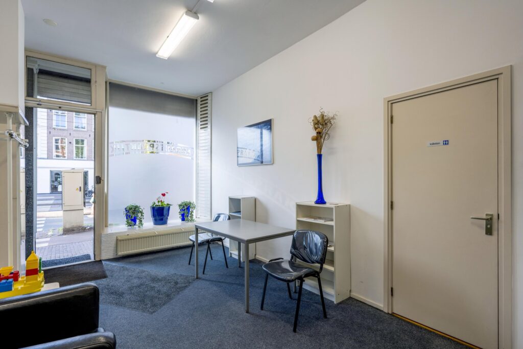 Small waiting area with two chairs, a table, and decorative elements inside a storefront on Overtoom.