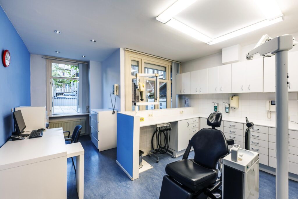Modern dental treatment room with a black dentist chair, blue and white interior, and medical equipment.