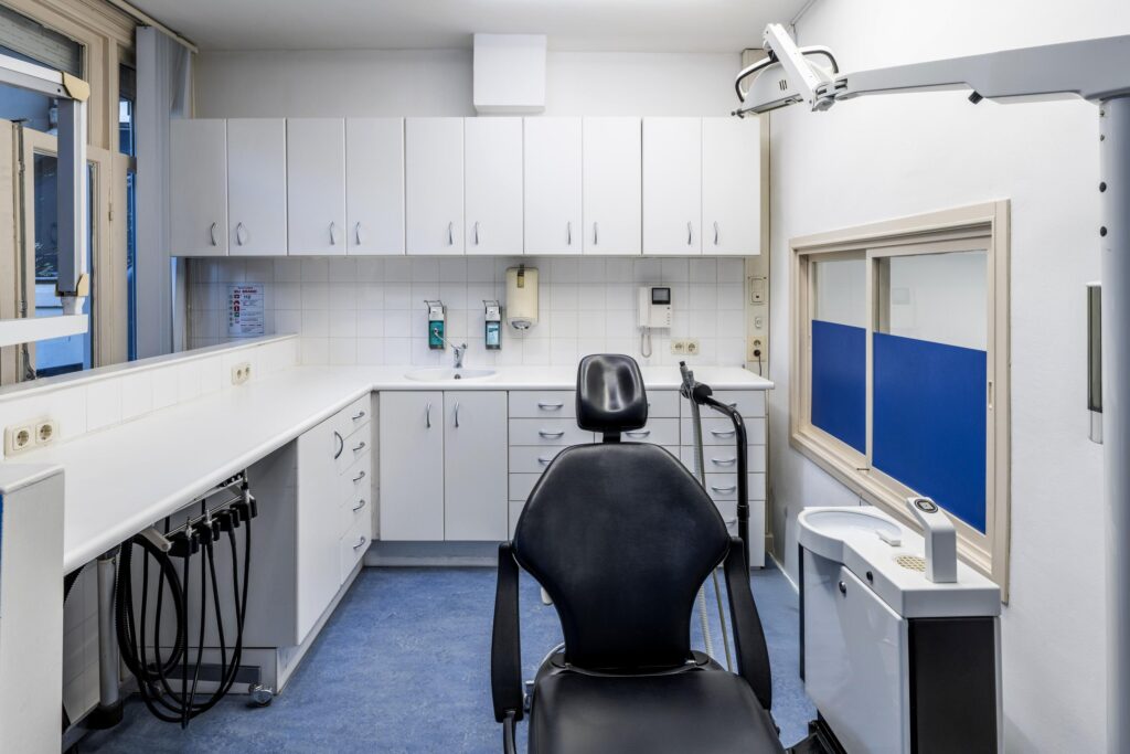 Modern dental treatment room with a black dentist chair, white cabinets, and medical equipment.
