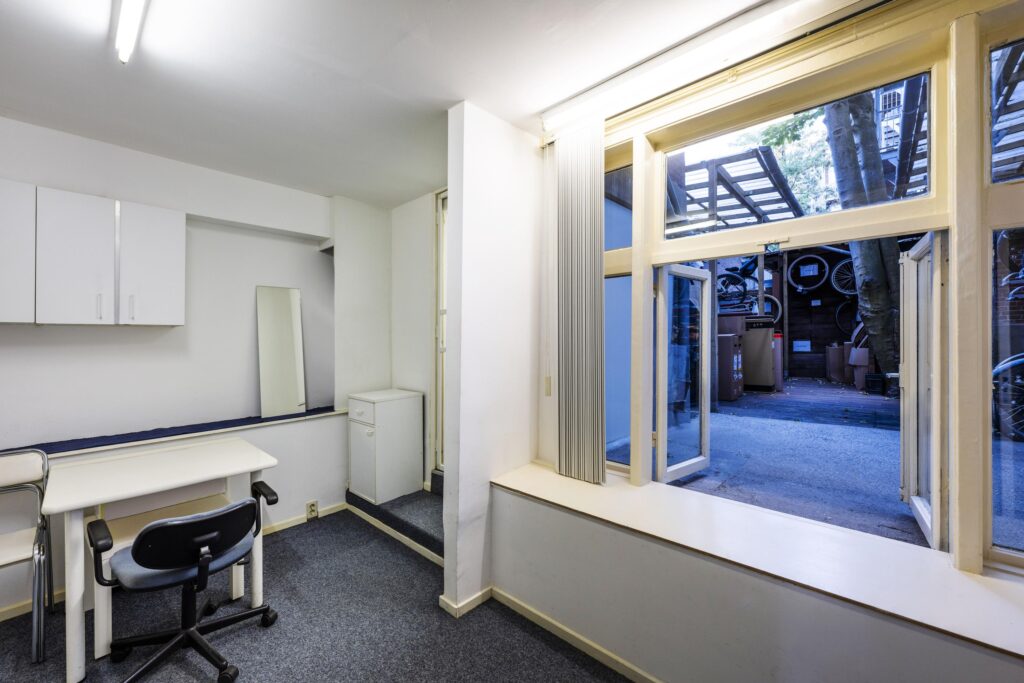 Simple office space with a desk, chair, and open window looking out onto a courtyard with bicycles.