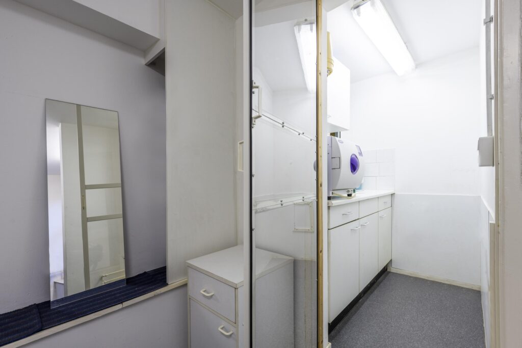 Small, white utility room with cabinets, a mirror, and a sterilization machine on the counter.