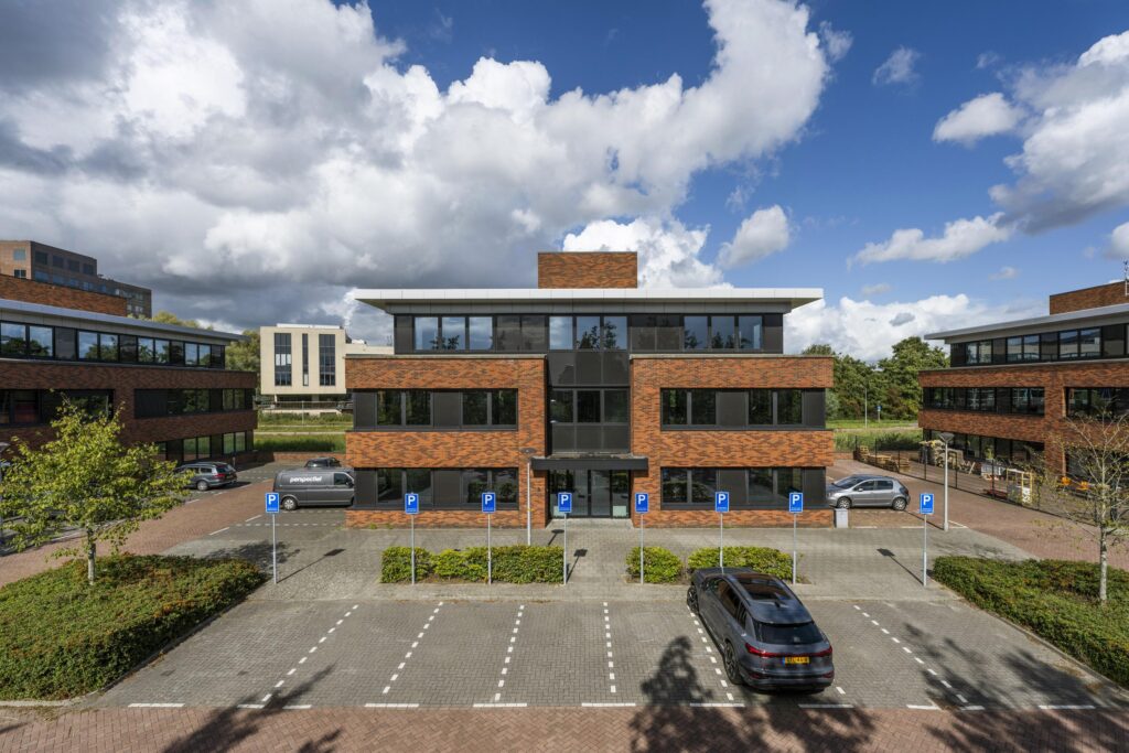 Modern office building on Veteranenlaan with adjacent parking spaces and cloudy blue sky.